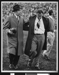 Notre Dame football coach Frank Leahy and University of Southern California football coach Jeff Cravath walking off the field together after game at Los Angeles Coliseum (full figure shots), 1947