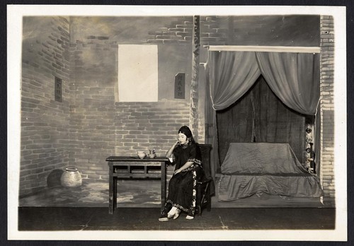 Woman of modest means is seated at a table next to a canopied bed, staged at the Great Star Theatre /
