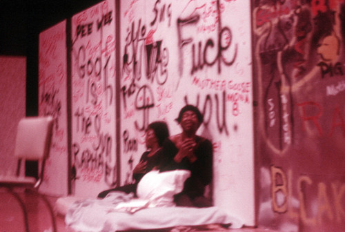 Play performance: two actors or dancers sitting against graffiti backdrop