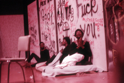 Performance: three actors sitting in front of graffiti backdrop