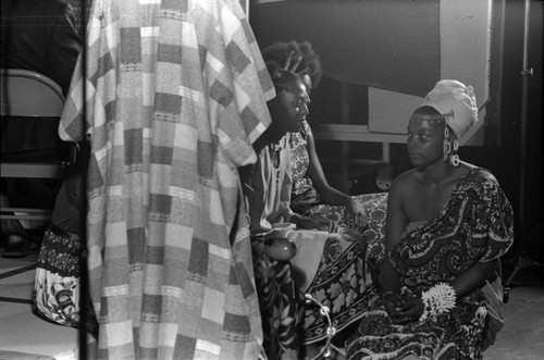 Figure in a checkered long robe standing next to three women