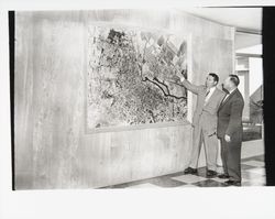 Gene Benedetti pointing at an aerial map in Petaluma City Hall, Petaluma, California, 1954