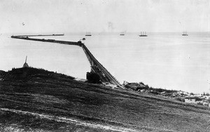 Breakwater under construction at the Port of Los Angeles, showing ships in the distance, ca.1900