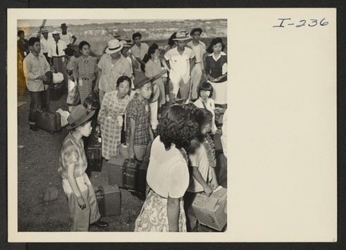Closing of the Jerome Center, Denson, Arkansas. Jerome residents with their hand luggage wait at the [illegible] car entrance for their names to be called by the W.R.A. official checking the list. Photographer: Iwasaki, Hikaru Denson, Arkansas