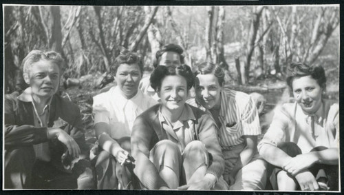 Photograph of a group of women sitting in front of a stand of trees near Manzanar