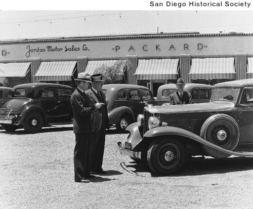 Three men standing around a Packard automobile at a Packard automobile dealership