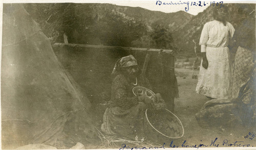 Elderly Native American woman seated with baskets at her home on the Potrero Reservation, later known as the Morongo Reservation
