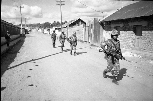 Armed soldiers walk through a neighborhood, Guatemala, 1982