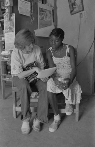 Nina S. de Friedemann and a woman looking at pictures, San Basilio del Palenque, ca. 1978