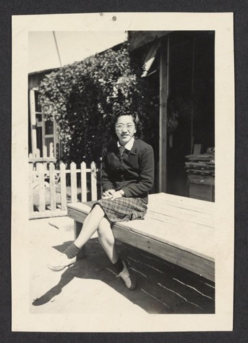 [Woman seated on bench at internment camp]