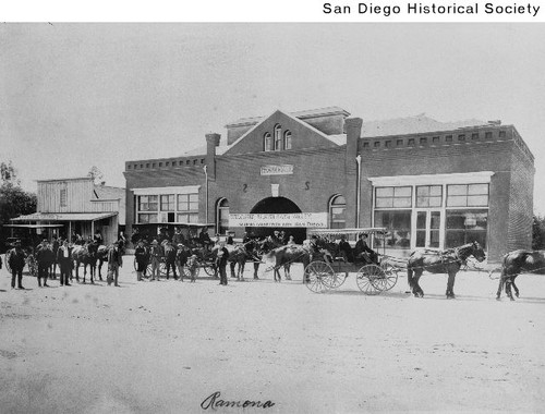 Men standing with horse-drawn carriages in front of the Ramona Town Hall
