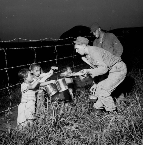 Soldiers giving food to Korean children through fence