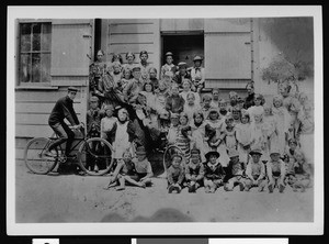 Group portrait of students at the Cahuenga Township School posing in front of a wooden schoolhouse