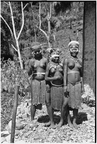 Adolescent girls (Kopi, Kanila, and Kena) smiling next to the Cooks' house in Kwiop