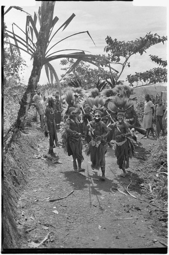 Bride price ritual: decorated men with spears charge in mock aggression, lead groom's group into the bride's village