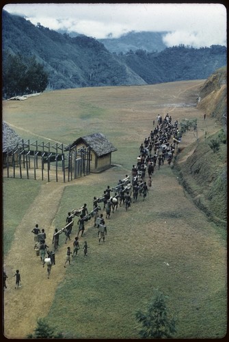 Tabibuga, line of men carry cargo past the jail building