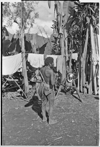 Men, one carrying an axe, in yard where laundry dries