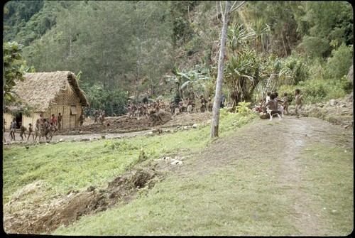 Children watch Ery Ben, crouching in center, disguised as mudman or clown