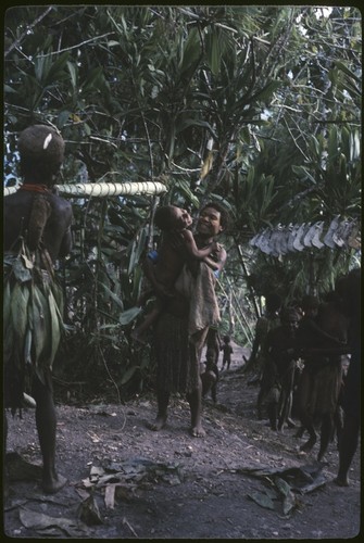 Pig festival, fertility ritual: deaf child and mother annointed with sacred water, pig jaws on cordyline in background