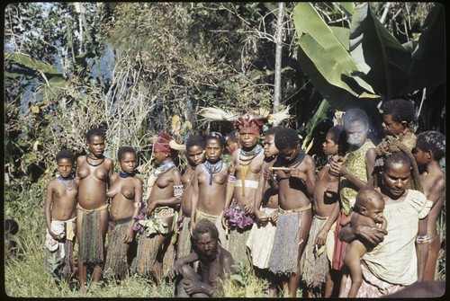 Bride price for Aina: payment, observed by group of children and young women, some wearing elaborate headdresses and other ornaments