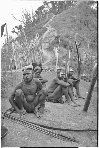 Men and boys with bows and arrows rest beside trail, sorcery gate in background