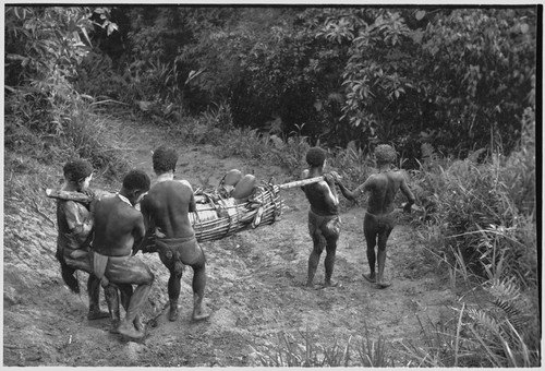 Mortuary ritual: women, their faces and bodies smeared with clay as sign or mourning, carry corpse wrapped for burial