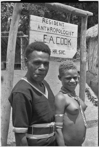 Man wearing police uniform, woman by sign near Cooks' house, "Resident Anthropologist, E.A. Cook, 24 Hr. Svc."