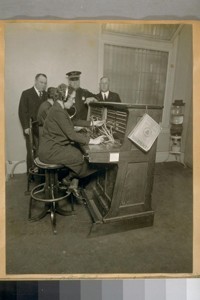 Switch Board of S.F. [San Francisco] Police Dept. Hall of Justice, 1922. L. to R.: Thos. F. Delwry of the Pacific Telephone & Telegraph co. And Chief of Police D.J. O'Brien. The operator on this end is Miss Grace Penn