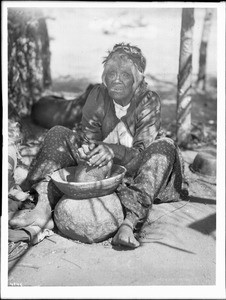 Maria Casseri, a Coahuilla Indian woman, grinding mesquite beans for flour on a stone metate with a basket top, California, ca.1899