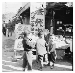 Three young children holding hands outside a shop, South Korea 1956-59