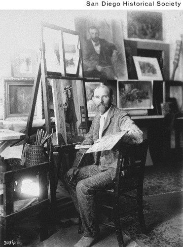 Charles A. Fries sitting at an easel and holding a pallet and brush inside his studio