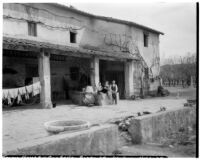 Man, woman and young boy sitting outside a farmhouse with a laundry line hung in the background, Italy, 1929