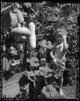 Three-year-old Rosita Dee Cornell standing next to a trellis with cucumber and squash growing on it, California, 1934