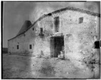 Two little girls sitting in the doorway of a large stucco barn, Spain, 1929