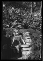 Rosita Dee Cornell standing by a rock wall in a garden, California, 1933