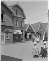 Two little girls wearing traditional Dutch clothing outside a row of buildings in Holland, 1929