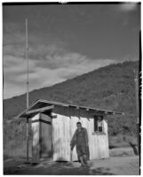 Unidentified man stands in front of small post office building, De Luz, 1937