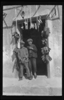 Two young boys standing in a doorway surrounded by hanging bundles of shoes, Europe, late 1920s