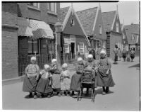 Group of seven little girls in traditional Dutch clothing on a shopping street, Holland, 1929