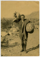 Ralph D. Cornell, holding bags, in desert