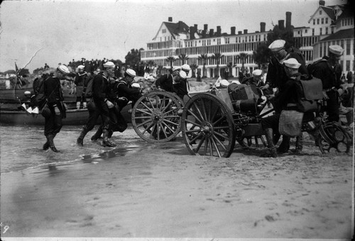 US Navy sailors practice amphibious maneuvers with cannons on beach in front of Hotel del Coronado, c. 1918