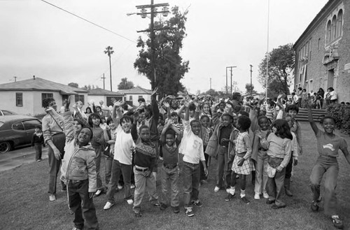 Ritter Elementary School children waving and pointing toward the sky, Watts (Los Angeles, Calif.), 1983