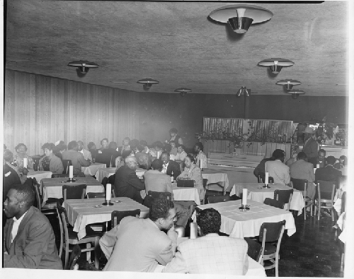 Men and women seated at white-cloth covered tables in one of dining rooms at Slim Jenkins Bar and Restaurant Oakland, California