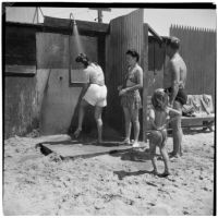 Two women, a man, and a young girl in line for the outdoor shower at the beach on Labor Day, Los Angeles, September 3, 1945