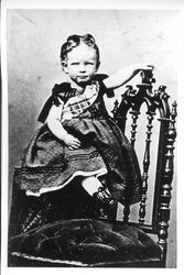 Martha J. Crow, daughter of James Rancon and Elizabeth Ann (Gilliam) Crow, as a young child of 1-2 years standing on ornate chair in long fancy dress