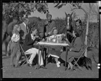 Actress Elissa Landi, family members, and friends having breakfast outdoors with horses and dog, [Los Angeles?], 1936