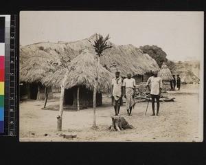 Men standing by fetish houses, Nigeria, ca. 1920