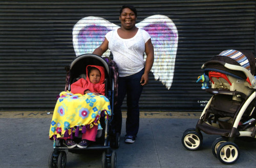 Unidentified woman and a child in stroller posing in front of a mural depicting angel wings