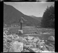 H. H. West stands atop a rock and fishes in the San Gabriel River, San Gabriel Canyon, about 1903