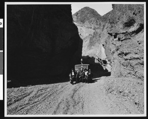 Three people sitting on the front of an automobile in Titus Canyon, Death Valley, ca.1900-1950
